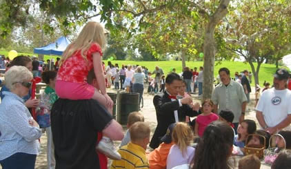 Little girl sits on the shoulders of her father to watch a magician perform in La Mirada